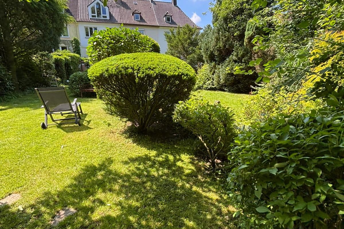 Sonniger Garten mit einer Sitzgelegenheit und gepflegten Gehölzen